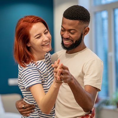 Joyful young diverse married couple dancing in living room at home, happy multiracial family man and woman having fun while spending time together indoors, having romantic date in studio apartment