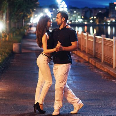 young couple dancing tango on the embankment of the river in the evening